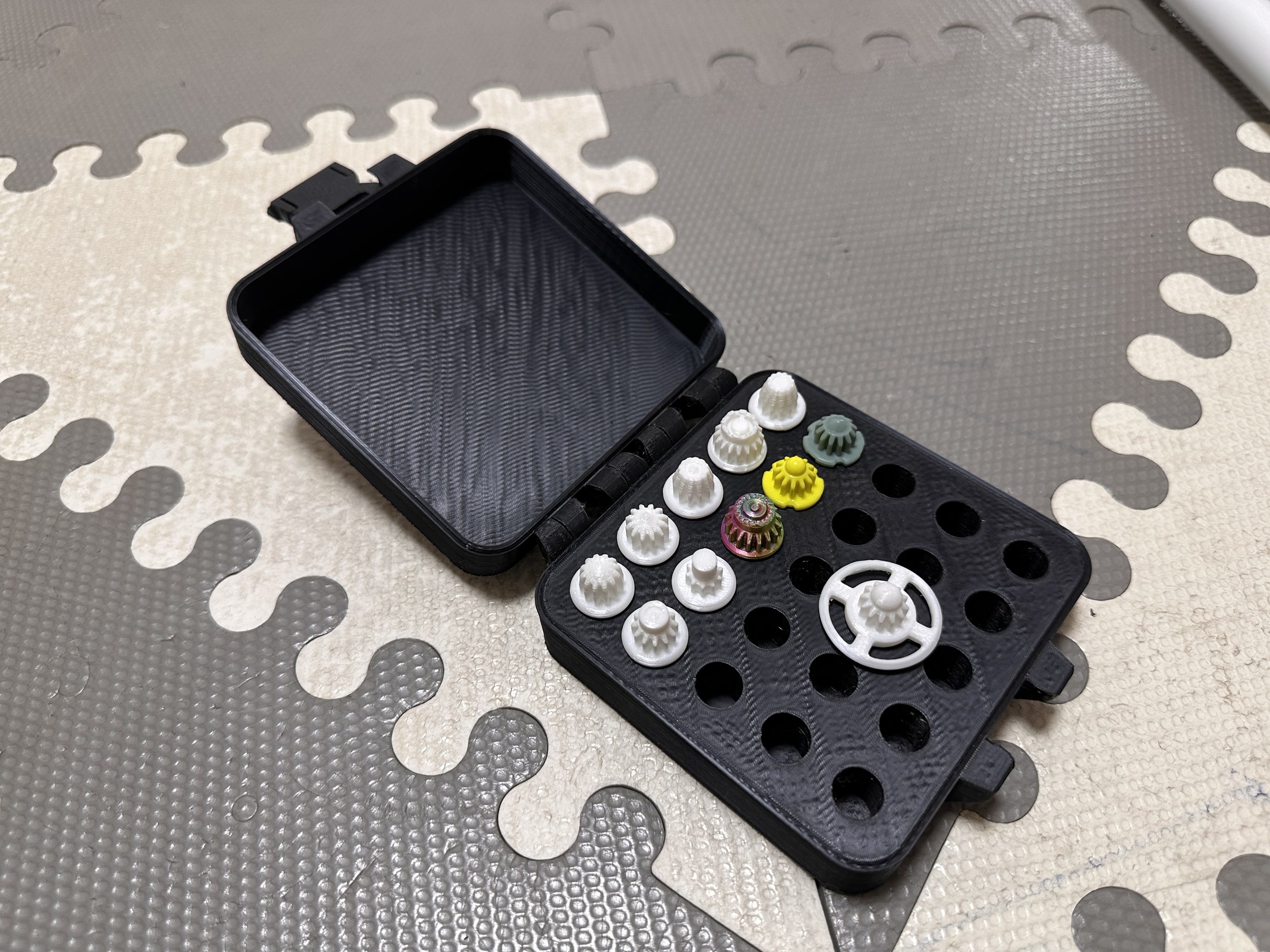 黒い3Dプリント製ケースに、複数のベイブレード用ビットを収納した状態。白、黄色、緑などのパーツを並べて保管できる